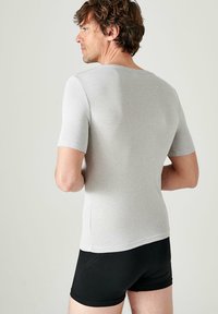 T-shirt a maniche corte, di colore grigio chiaro, realizzato in tessuto morbido, design aderente, texture minima, indossato con pantaloni corti neri. Vista posteriore, finitura semplice.