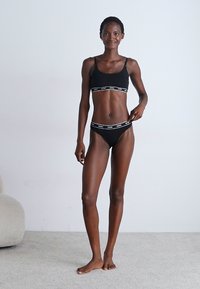 Black crop top with a wide elastic band featuring white text, paired with matching black bikini briefs. Smooth fabric and minimalistic design.