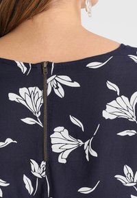 Merihenkinen paita, jossa on valkoinen kukkakuosi, selässä huomaamaton vetskari ja sileä kangas. Yksinkertainen pyöreä pääntie.