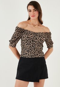 Halenka s leopardím vzorom bez ramienok z mäkkej látky s krátkymi pufovanými rukávmi, skombinovaná s čiernou sukňou v zavinovacom štýle.