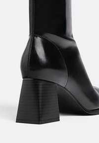 Schwarze Leder-Ankle-Boots mit glänzender Oberfläche, Blockabsatz mit vertikalen Rillen und einem glatten, runden Zehendesign.
