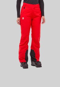 Pantalons de ski rouges en matériau imperméable, avec une coupe fuselée, des accents noirs sur les jambes et un logo sur le devant.