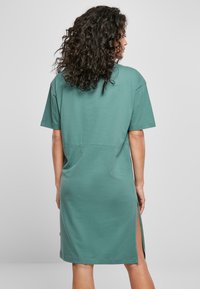 Groene katoenen T-shirtjurk met korte mouwen, zijzakken en een losse pasvorm. Gladde textuur, eenvoudig ontwerp en kniehoog.