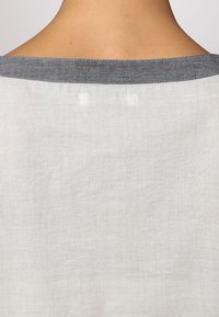 Top in lino grigio chiaro con una texture morbida e un colletto grigio scuro simile al denim. Il design è semplice con cuciture minime visibili.