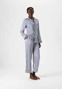 Dryžuotas medvilnės pižamų komplektas tamsiai mėlynos ir baltos spalvos, turintis mygtukais užsegamą viršų su apykakle ir kelnes su tiesiu sijonu bei užlenktais kulkšnies kraštai.