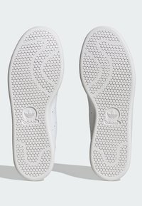 Valged spordijalatsid, millel on tekstuuriga kummist tallad, millel on kuusnurksete mustritega. Brändi logo on esindatud kannarea piirkonnas. Sile ülapind.