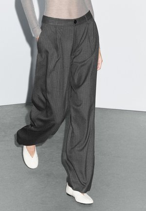 Dark grey pinstriped trousers with a relaxed fit, featuring side pockets and a front button closure, paired with white textured shoes.