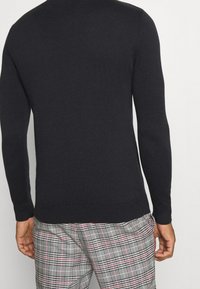 Marinblå tröja med långa ärmar, stickad textur, rundad halsringning, figursydd design. I kombination med grå rutiga byxor med röda detaljer.