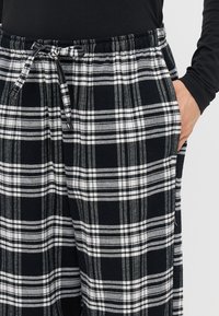 Sorte og hvide ternede pyjamasbukser lavet af blødt stof, med en elastisk talje og snøre samt sidelommer.