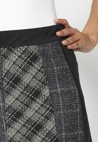 Jupe à carreaux avec une taille noire et un motif à carreaux gris avec des accents blancs. Le tissu a une apparence texturée avec un aspect tissé.
