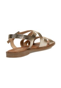 Sandalias de cuero dorado con diseño entrelazado, parte trasera abierta y suela de goma plana. Parte superior texturizada con un ligero brillo.