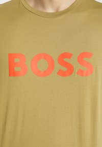 Olivově zelené bavlněné tričko s odvážným červeným logem "BOSS". Tkanina má hladkou texturu a klasický design s kulatým výstřihem.