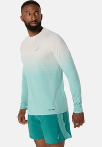 Lätt långärmad idrottströja med en gradientdesign i ljusblått och mintgrönt, med reflekterande logotyp, kombinerad med matchande teal-färgade shorts.