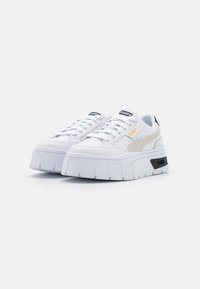 Vita plattformssneakers med en texturerad gummisula, med perforerade sidopaneler, svarta accenter och en metallisk logotyp på tungan.