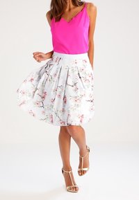 Haut rose sans manches avec encolure festonnée, assorti à une jupe blanche à motif floral avec des fleurs roses. Sandales à lanières beige clair.