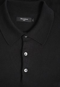 T-shirt polo noir en tissu tricoté, avec un col classique, trois boutons en métal argenté et une étiquette indiquant la taille L.