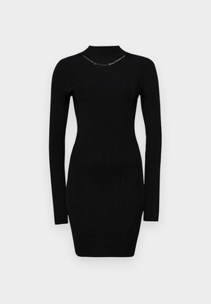 Črna rebrasta obleka z dolgimi rokavi in visokim ovratnikom, ki se prilega telesu, z srebrnimi detajli na ovratniku. Preprost in prilegajoč se dizajn.