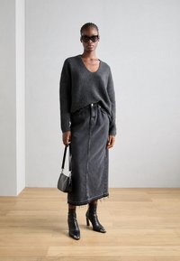 Dunkelgrauer Strickpullover mit V-Ausschnitt, kombiniert mit einem langen schwarzen Jeansrock mit ausgefransten Kanten. Schwarze Ankle-Boots mit spitzen Zehen runden den Look ab.