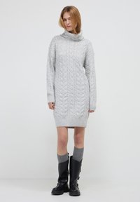 Abito in maglia a trecce grigio con collo alto a cowl, maniche lunghe e polsini a coste, abbinato a stivali neri fino al ginocchio e calzini grigi.