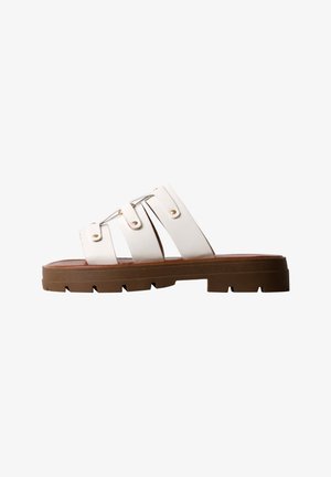 Sandale slide en cuir blanc avec trois brides et rivets dorés, semelle épaisse en caoutchouc marron avec un motif de semelle profond.