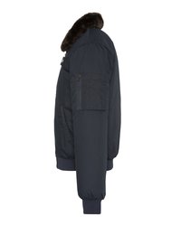 Ciemnoniebieska kurtka bombowa z prążkowanymi mankietami i dolnym brzegiem, z zamkniętą kieszenią na rękawie oraz brązowym kołnierzem z futra syntetycznego, przedstawiona z boku.