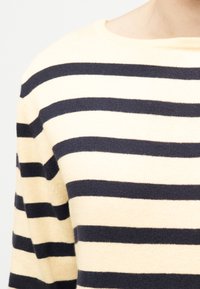 Gros plan sur un pull crème avec des rayures noires horizontales uniformément espacées sur la poitrine et les épaules.