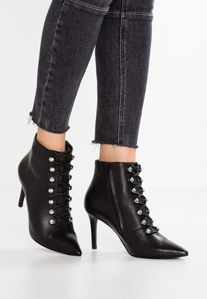 Bottines noires à bout pointu et talons hauts, avec lacets à l'avant et fermeture éclair latérale, portées avec un jean skinny noir effiloché.