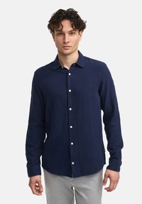 Marineblaue Langarmbluse aus strukturiertem Stoff, mit Button-Down-Kragen und weißen Knöpfen; verfügt über dezente Branding-Elemente auf der Brust.