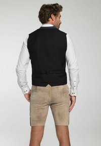 Schwarze Weste mit strukturierter Oberfläche, kombiniert mit hellbeigen Shorts. Das weiße Hemd hat knöpfbare Manschetten und einen dekorativen Kragen.