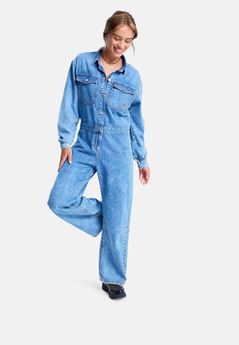Hellblauer Jeans-Overall mit langen Ärmeln, zwei Brusttaschen und tailliertem Schnitt. Verfügt über ein weites Bein-Design und eine Knopfleiste auf der Vorderseite.