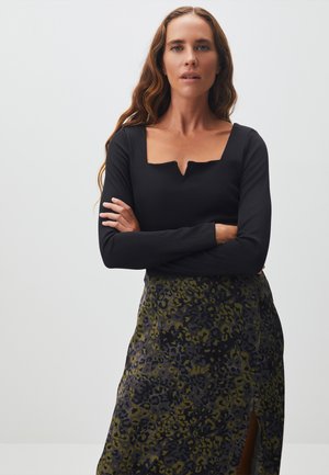 Zwarte lange mouw top met een vierkante halslijn; gecombineerd met een rok met groen en zwart luipaardprint met een zijsplit. Glad textuur, getailleerd ontwerp.
