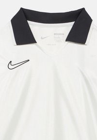 Λευκό πόλο μπλουζάκι Nike Dri-FIT με μαύρο γιακά και μαύρο κεντημένο λογότυπο στο αριστερό μέρος, με ομαλή, ελαφριά υφή.
