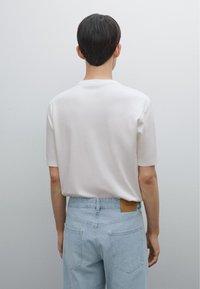 Hvid kortærmet t-shirt; blødt bomuldsstof. Parret med lyseblå denim jeans, der har en tan læderlap på den bagerste talje.
