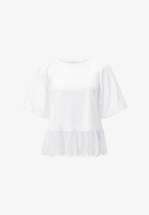 Fehér blúz széles, könyékig érő ujjakkal és csipkével szegélyezett szegéllyel, kerek nyakkivágással és bő, laza fazonnal.