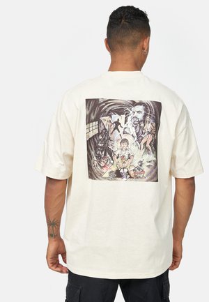 Cremefarvet t-shirt med tryk på ryggen, der viser en farverig, detaljeret illustration af forskellige karakterer og scener.