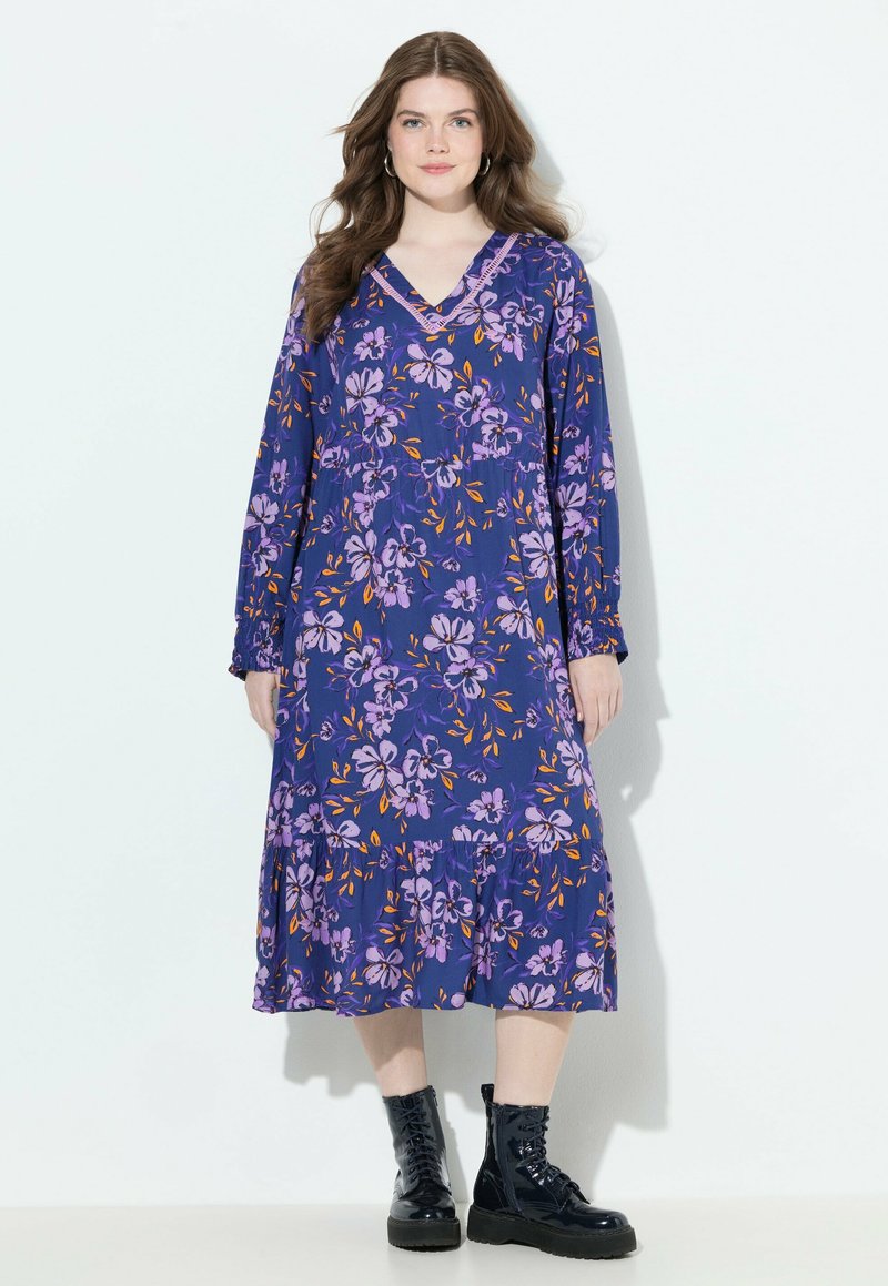 Blumen Kleid in tiefem Lila mit langen Ärmeln, V-Ausschnitt und geraffter Taille. Es hat helllila und orangefarbene Blumen sowie einen gestuften Saum.