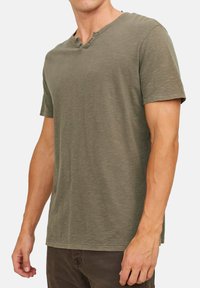 Olijfgroene t-shirt met korte mouwen, een henley hals en een drieknoopsluiting. Heeft een zachte, gestructureerde stof en een ontspannen pasvorm.