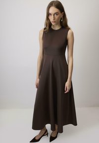 Rochie maro fără mâneci, cu un corset ajustat și fustă evazată, dintr-un material neted. Purtați cu încălțăminte cu vârf ascuțit de culoare neagră.