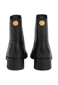 Gli stivaletti neri in pelle presentano una texture liscia, punta rotonda e un accento in hardware dorato sul retro. Tacco corto a blocco per la stabilità.