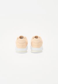 Baskets pêche clair avec une texture lisse, semelles en caoutchouc blanches et accents en mesh au niveau du talon, avec un logo en relief à l'arrière.