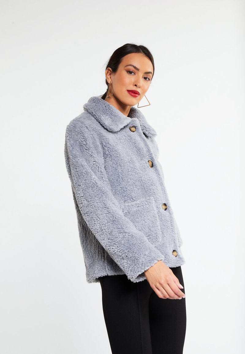 Grå faux fur jakke med krave, to frontlommer og guldtonede knapper. Har en blød, tekstureret overflade og en afslappet pasform.