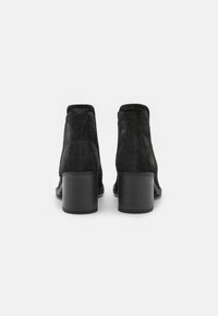 Sorte ruskindsstøvler med rundet tå, mellemhøj ribbet hæl og en glat krave, der har et minimalistisk design og struktur.