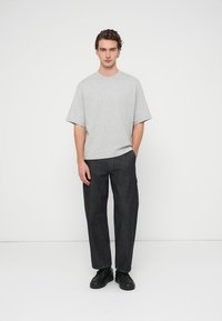 Γκρι κοντομάνικο μπλουζάκι σε χαλαρή γραμμή συνδυασμένο με σκούρο τζιν παντελόνι, με απλό σχέδιο, φορεμένο με μαύρα αθλητικά παπούτσια.