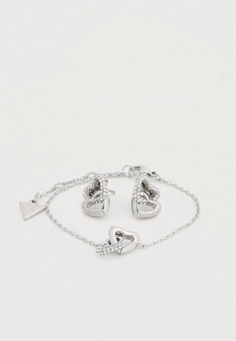 Σετ ασημένια κοσμήματα που περιλαμβάνει σκουλαρίκια σε σχήμα καρδιάς διακοσμημένα με στρας και ταιριαστό βραχιόλι, και τα δύο με αλυσίδες καλωδίου.