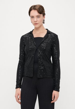 Czarna długa kurtka z długim rękawem, ozdobiona cekinami, z wyciętym kołnierzem i zapięciem z przodu, w zestawieniu z czarnym topem i fakturowanymi czarnymi spodniami.