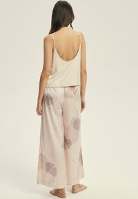 Zestaw piżamowy składający się z miękkiego różowego satynowego topu na ramiączkach z dekoltem z tyłu oraz spodni o szerokich nogawkach ozdobionych dużymi kwiatowymi wzorami w stonowanych odcieniach.