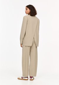 Beige ribbed blazer with a split back, paired with wide-leg pants. White sneakers with maroon accents complete the ensemble.