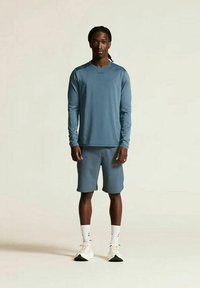 Das sportliche Outfit besteht aus einem langärmeligen, hellblauen Oberteil und passenden Shorts, gefertigt aus atmungsaktivem Stoff. Die Accessoires umfassen weiße Socken und Schuhe.