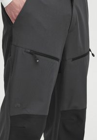 Pantalones ligeros negros con bolsillos con cremallera, con material texturizado y cinturilla ajustable. Incluye un sutil branding en la pierna.