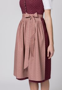 Das Oberteil besteht aus dunkelrotem Stoff mit kleinen weißen Bollenkreis; der Rock ist rosa mit vertikalen Streifen und floralen Akzenten, gebunden mit einer Schleife.